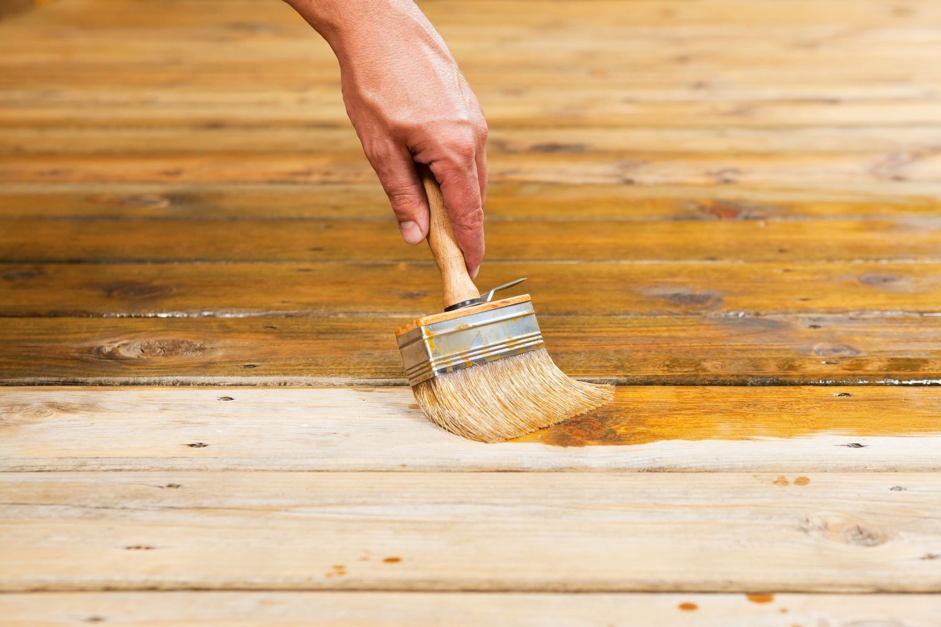 Applying timber deck stain with a paintbrush as part of deck maintenance